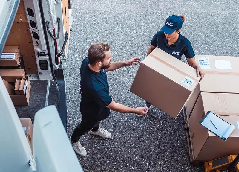 Couriers loading labeled cartons from a pallet into a delivery van